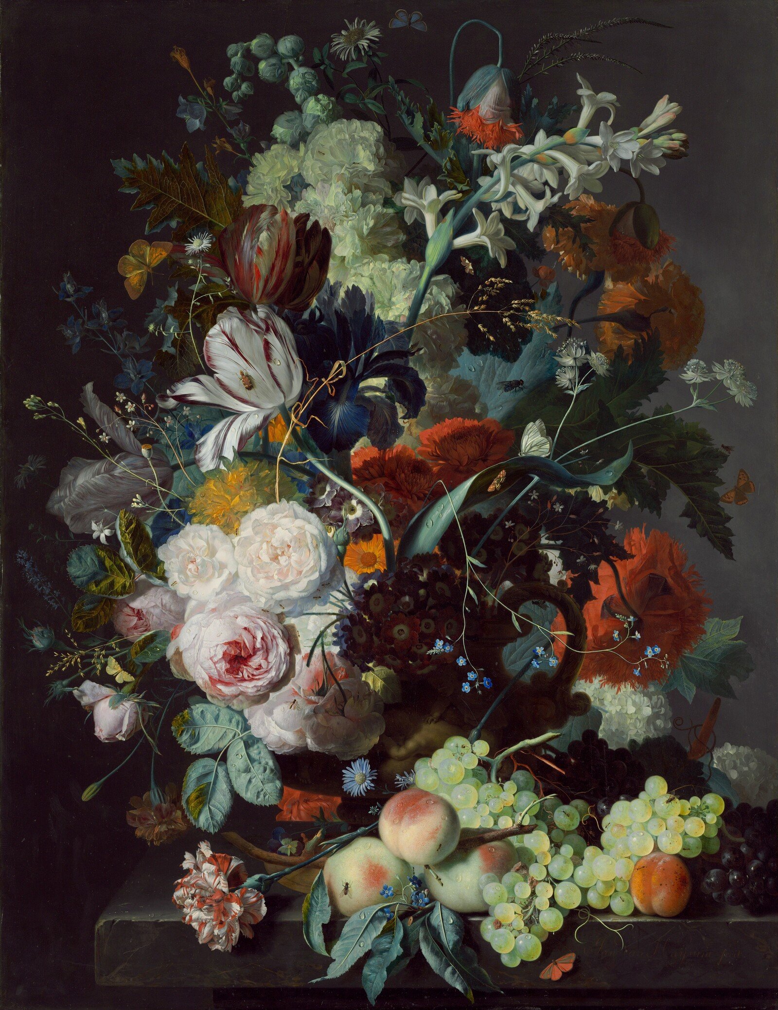 A dense bouquet of many flowers rises from a vase above peaches and grapes against a dark background.